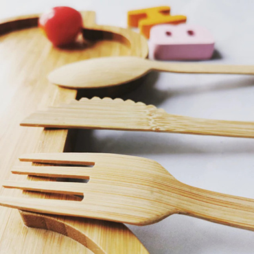 A close-up of a biodegradable bamboo fork, knife, and spoon on a wooden tray, highlighting their natural texture.