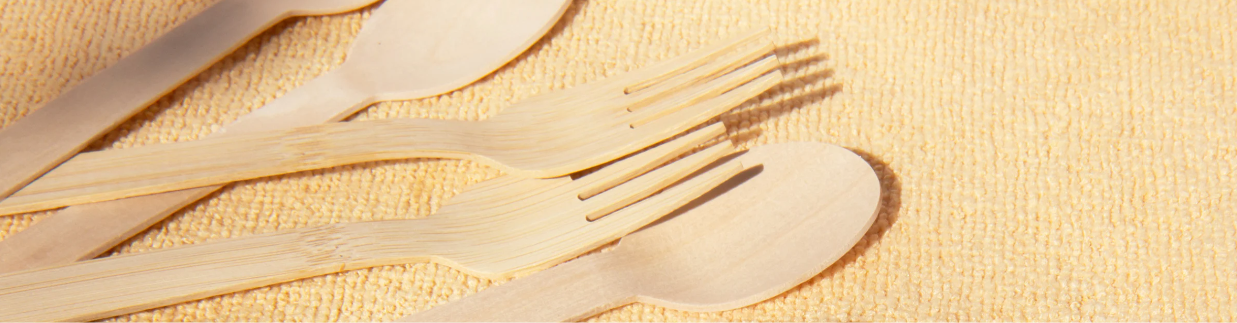 Eco-friendly bamboo forks, knives, and spoons on a beige textured background