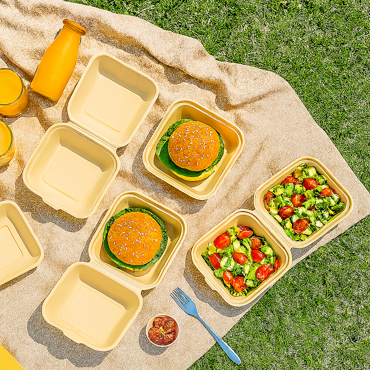 Eco-friendly bamboo fiber clamshell food containers with burgers and salad on a picnic setup
