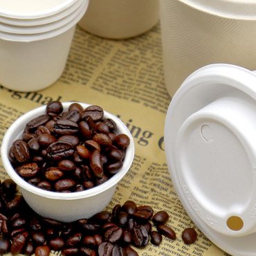 Bamboo fiber disposable coffee cups with compostable lids and roasted coffee beans on newspaper background.