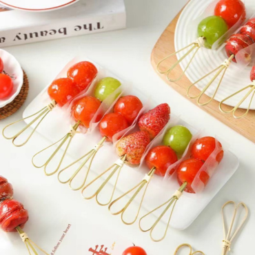Bamboo knot skewers used for serving candied fruits (sugar-coated strawberries and tomatoes) arranged on a white plate.