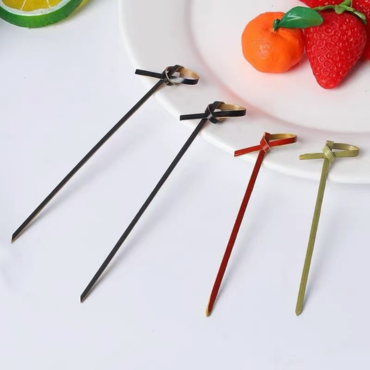 Colorful bamboo knot skewers in black, red, and natural bamboo designs, used to serve fruits like strawberries and oranges.