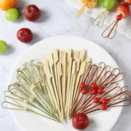 Colorful bamboo skewers in green, red, and natural shades with fruit displayed on a white plate.