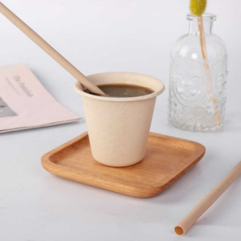 Disposable bamboo straw in a takeaway coffee cup on a wooden tray