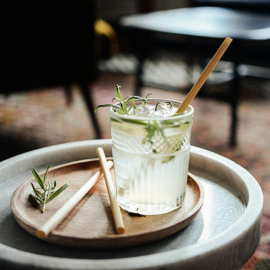 Disposable bamboo straw in a cocktail with herbs and ice on a wooden tray