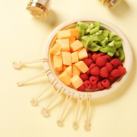 Cartoon-topped bamboo paddle skewers used to serve colorful fruit chunks in a compostable bowl.