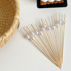 Elegant bamboo skewers with pearl tops arranged on a white surface, ideal for upscale catering and dessert presentation.